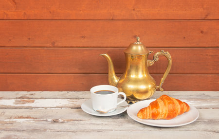 Cup of coffee, coffee pot and croissant on aged wooden table. view with copy space.の写真素材
