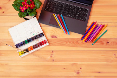 Color pencils, watercolor paints, primrose flower and laptop on desk. Top view, copy space.の写真素材