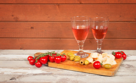 Two glasses of rose wine, cherry tomatoes, green olives and pieces of cheese on aged wooden table. view with copy space.の写真素材