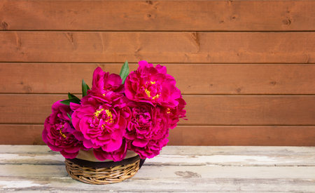 Beautiful red peony flowers in wicker basket on aged wooden table. view with copy space.の写真素材