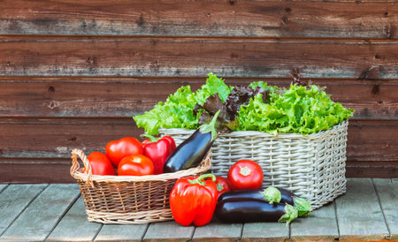 Fresh vegetables and colorful salad leaves in wicker baskets on rustic wooden table.の写真素材