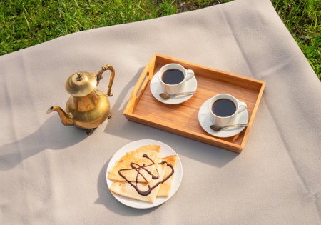 Coffee pot, coffee cups and pancakes with chocolate syrup on plaid on green grass. top view.の写真素材