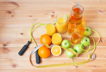 Apple juice, orange juice, oranges, apples, jumping roap and measuring tape near on wooden table. top view.の写真素材