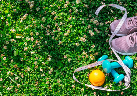 Sneakers, dumbbells, orange and measuring tape on fresh green grass. Healthy lifestyle concept. Top view, copy space.の写真素材