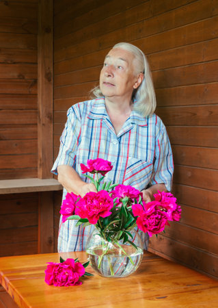 Senior woman arranging red peonies into glass vase. vertical shot.の写真素材