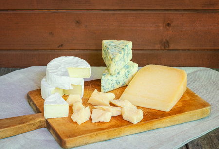 Various types of cheese on cutting board on rustic wooden table.の写真素材