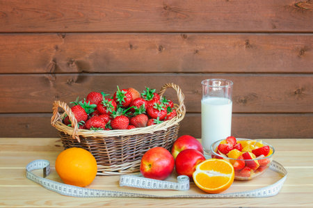 Yogurt, healthy fruit salad made of strawberry, oranges and nectarines, fresh oranges and nectarines near, wicker basket of fresh strawberry, and measuring tape on wooden table. Healthy eating concept.の写真素材