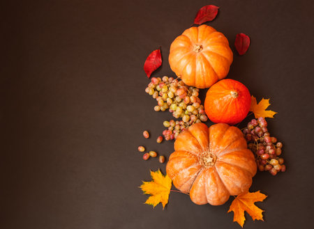 Border made of pumpkins, autumn leaves and grapes on dark background. Top view, copy space.の写真素材