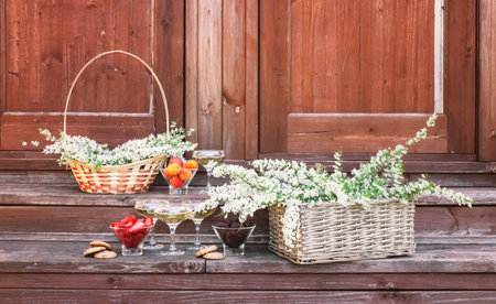 Spirea flowers in wicker baskets, fresh fruits, truffle candies, cookies and glasses of beverage are on steps of rustic wooden ladder.の写真素材