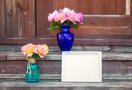 White frame and bouquets of roses in vases are on steps of rustic wooden ladder. View with copy space.の写真素材