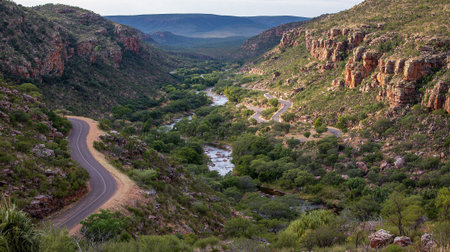 Scenic mountain pass road winds through verdant landscape beside a sparkling riverの素材