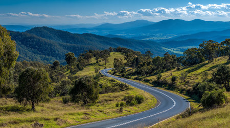 Serpentine Road Through Lush Green Hills and Mountains under a Blue Skyの素材