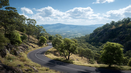 Scenic winding road through rolling hills, majestic mountains, and cloudy blue skyの素材
