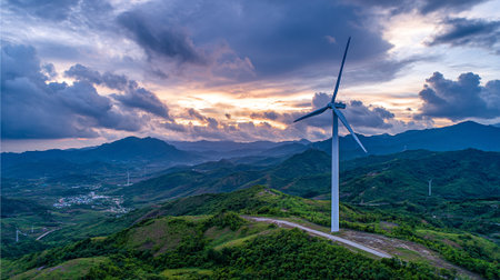 Striking wind turbine against a dramatic sunset over rolling green hillsの素材