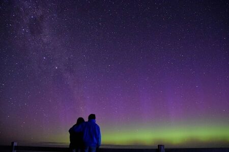 A couple observing a great display of Aurora Australis at Waipapa Point, New Zealand.の写真素材