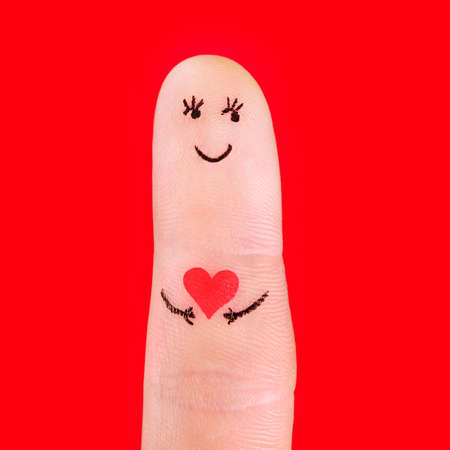 man in love concept - a man with red heart, painted at finger isolated on red backgroundの写真素材