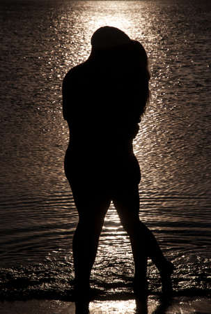 Young couple hug silhouette on a sea beach against sunset backgroundの写真素材