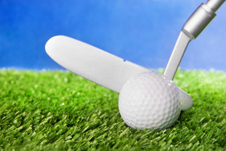 Golf ball and club on green field grass against blue sky - horizontal image