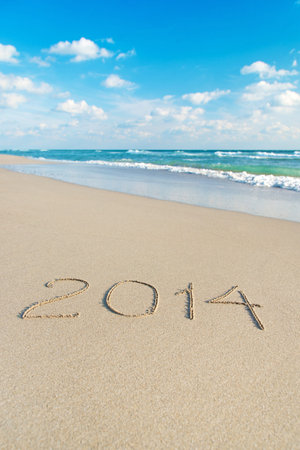 inscription 2014 on sea sand beach with the sun rays against wave foam and sky - vacation concept