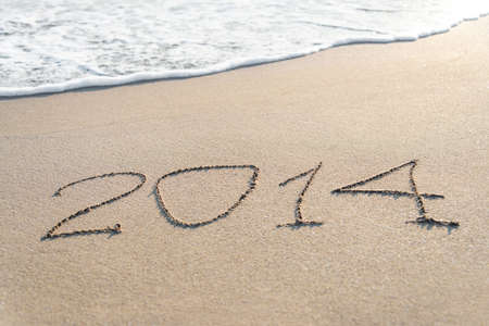 inscription 2014 on sea sand beach with the sun rays against wave foam and sky - vacation conceptの写真素材