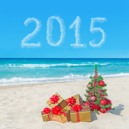 Christmas tree and golden gift boxes with big red bow on sea beach. Concept for New Year 2015 cards or calendarの写真素材