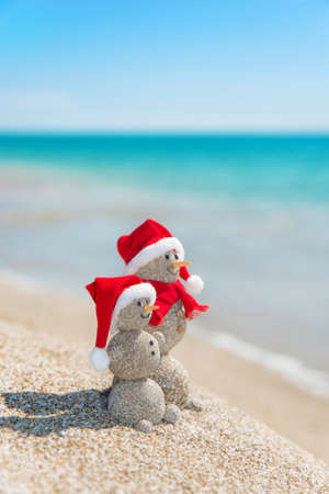 Smiley sandy snowmans couple at sea beach in christmas hat. New years holiday in hot countries concept.の写真素材