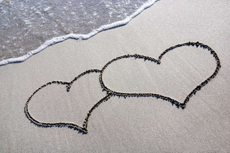 heart outline on the wet brilliance beach sand against waveの写真素材