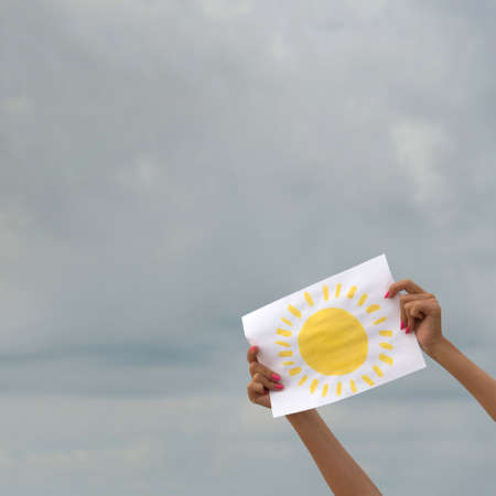 human hands with sheet of paper with sun image against overcast sky - positive thinking conceptの写真素材