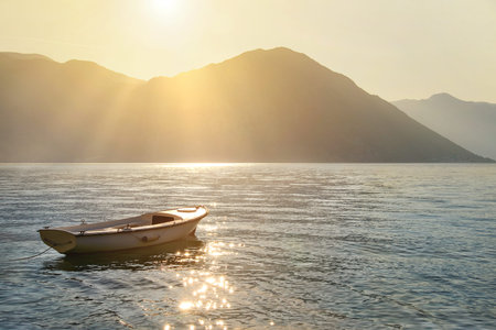 Fishing boat on moorage at sunlight glittering sea surface against sunset Lovcen mountain background with sun rays. Montenegro, Kotor Bay (Boka Kotorska).の写真素材