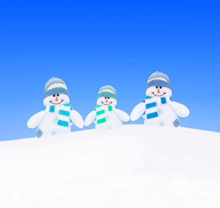 Happy amusing winter snowmen family (mother, father and child) or friends in knitted scarfs and hats at white snow against blue sky background - winter holidays greeting card conceptの写真素材