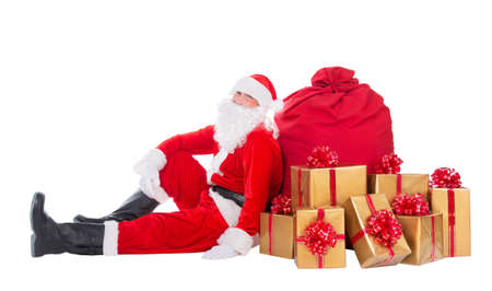 Santa Claus relax sitting near big red Christmas sack full of golden  presents, gifts and surprises isolated on white background, New Year or xmas holiday conceptの写真素材