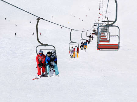 Chairlift (ski lift) transport skiers and snowboarders up a snowy downhill at winter ski snow Alpine resort, active seasonal outside sports backgroundの写真素材