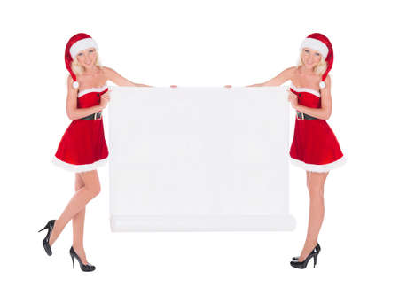 Two happy cute blonde cheerful Santa women with christmas white paper scroll advertising poster isolated on white backgroundの写真素材