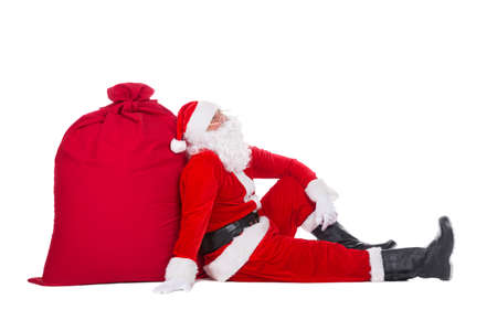 Santa Claus have rest sitting near big Christmas sack full of presents, gifts and surprises isolated on white background, New Year or xmas holiday conceptの写真素材