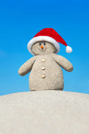 Positive creative sandy snowman in red Santa hat at beach. New Year and Christmas holiday travel destinations in hot countries conceptの写真素材