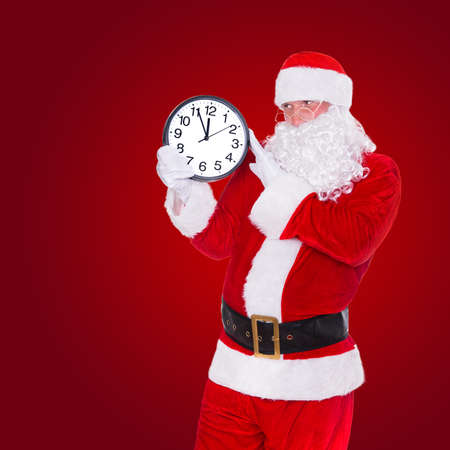 Christmas Santa Claus pointing at clock showing five minutes to midnight on red background. Happy New Year concept. の写真素材