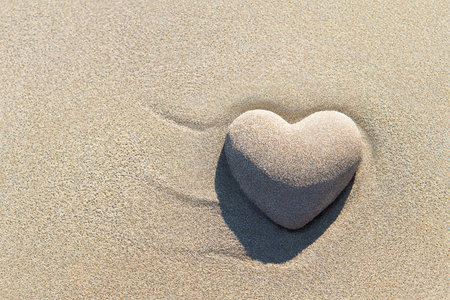 Heart made of sand with shadow on sandy beach background, Saint Valentines day greeting cards, romantic, love, honeymoon, proposal or wedding concept.の写真素材