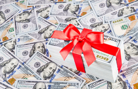 Gift  with big red bow ribbon made of united states dollars currency bundle on many new one hundred...