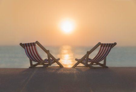 Two striped red-white sunbeds at sandy tropical sunset ocean beach. Natural travel background....