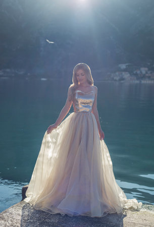 A dreamy enchanted fairy-tale princess in front of a mountain, seagull bird and sea in sunny beamsの写真素材