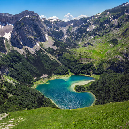 Trnovacko Lake, Montenegro, Durmitor National Park. Small mountain glacial romantic lake in the shape of a heart, surrounded with snowy rocky peaks and green forests.の写真素材