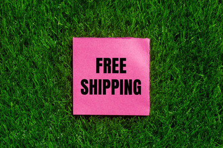 Free shipping message written on ripped torn pink paper with green grass background. Conceptual free shipping symbol. Copy space.の写真素材
