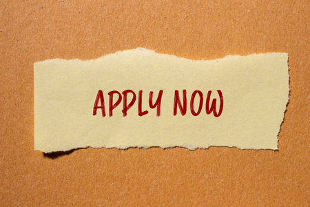 Apply now message written on ripped paper piece with cardboard background. Conceptual apply now symbol. Copy space.の写真素材