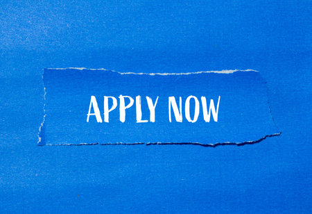 Apply now message written on ripped paper piece with blue background. Conceptual apply now symbol....