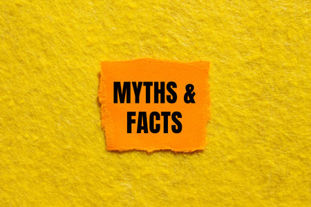 Myths and facts message written on ripped torn orange paper piece with yellow background. Conceptual...