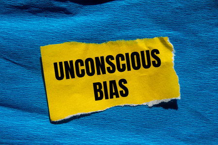 Unconscious bias message written on ripped torn yellow paper piece with blue background. Conceptual...