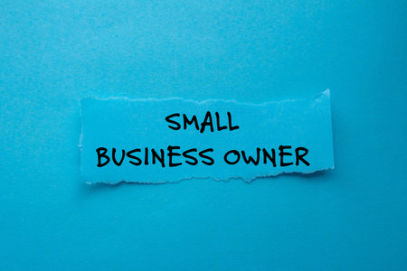 Small business owner message written on torn torn paper piece on blue background. Conceptual small...