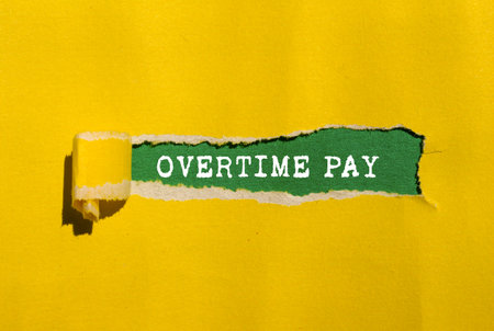 Overtime pay message written on torn yellow paper on green background. Conceptual overtime pay symbol. Copy space.の写真素材