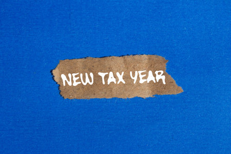 New tax year message written on ripped torn brown paper piece on blue background. Conceptual new tax year symbol. Copy space.の写真素材