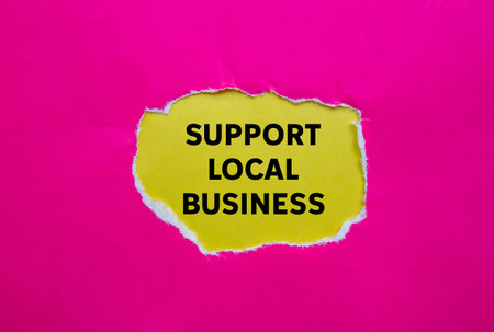 Support local business message written on ripped torn pink paper on yellow background. Conceptual support local business symbol. Copy space.の写真素材